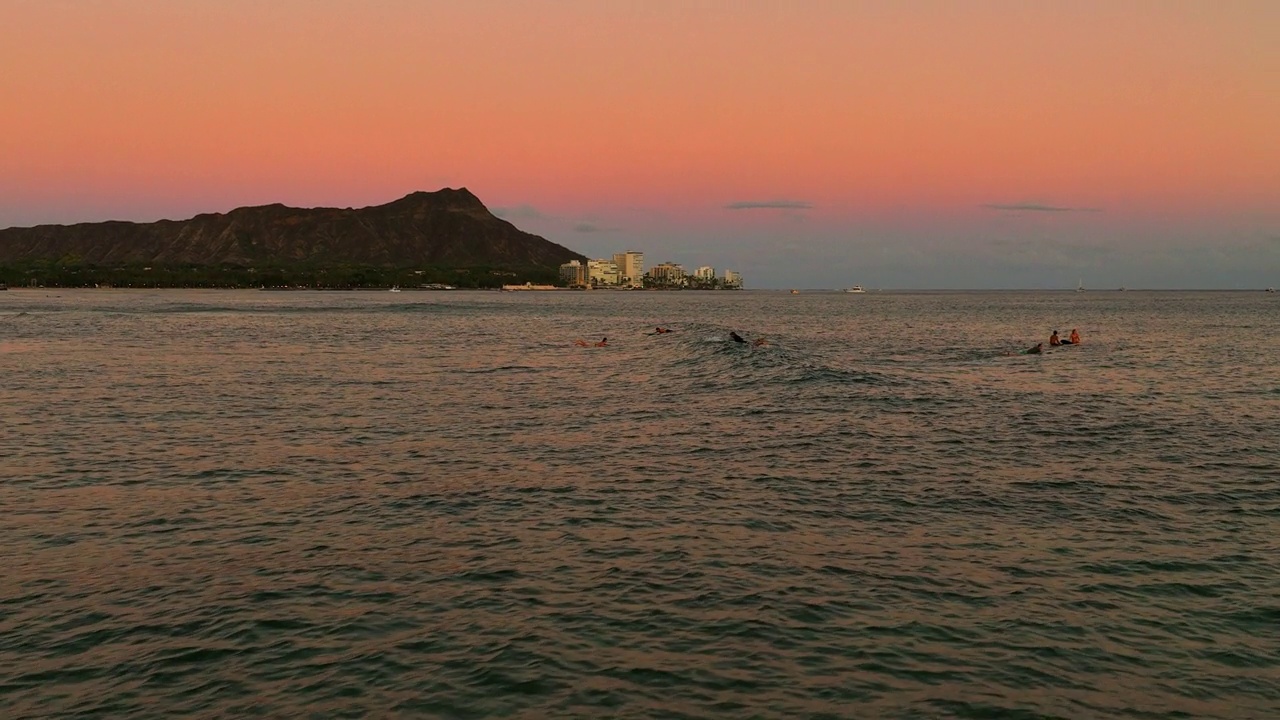 航拍:人们在瓦胡岛海边冲浪的慢动作镜头，日落时无人机向后飞行——夏威夷威基基视频素材