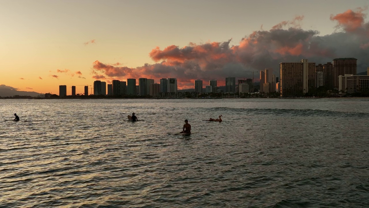 慢动作锁定镜头的人漂浮在海上的建筑物在城市在多云的天空下日落-威基基，夏威夷视频素材