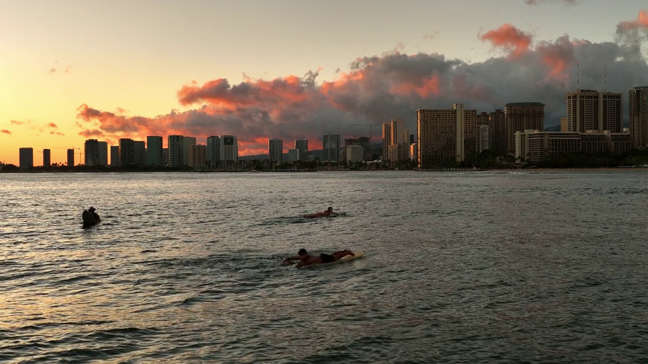 慢镜头的人游泳与冲浪板海浪在建筑物在住宅城市在日落-夏威夷威基基视频素材