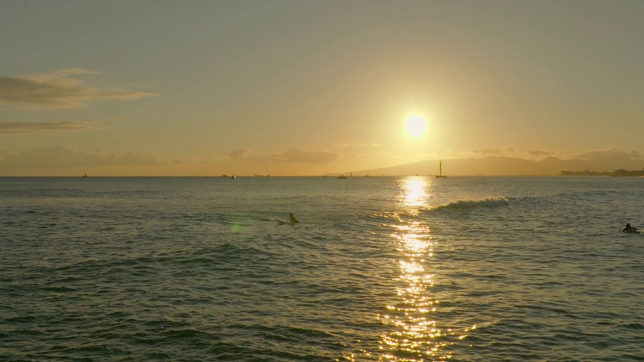 在夏威夷怀基基，夕阳下度假时，男子举起双手在海浪中冲浪的慢镜头视频素材