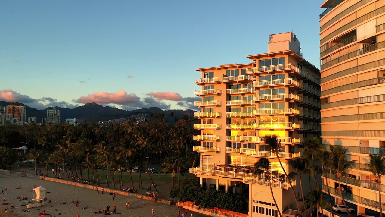 空中平移拍摄的酒店建筑和棕榈树在海滩日落-瓦胡岛，夏威夷视频素材