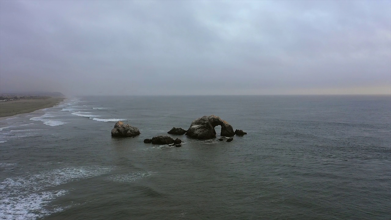 空中平移拍摄的岩石在海浪的海在海滩，无人机在多云的天空下向前飞行-旧金山，加利福尼亚视频素材