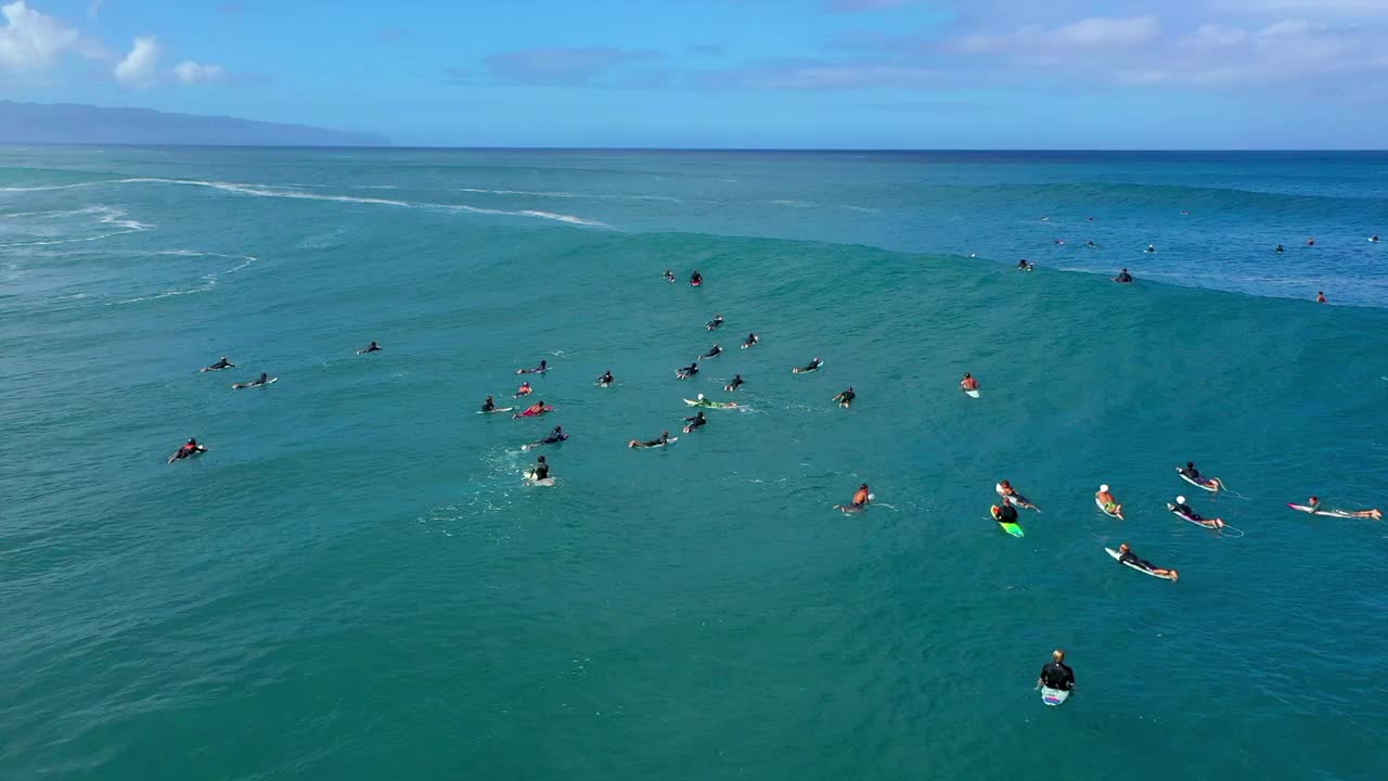 空中向后拍摄的男人和女人在云下的海浪上冲浪板游泳-夏威夷威基基视频素材