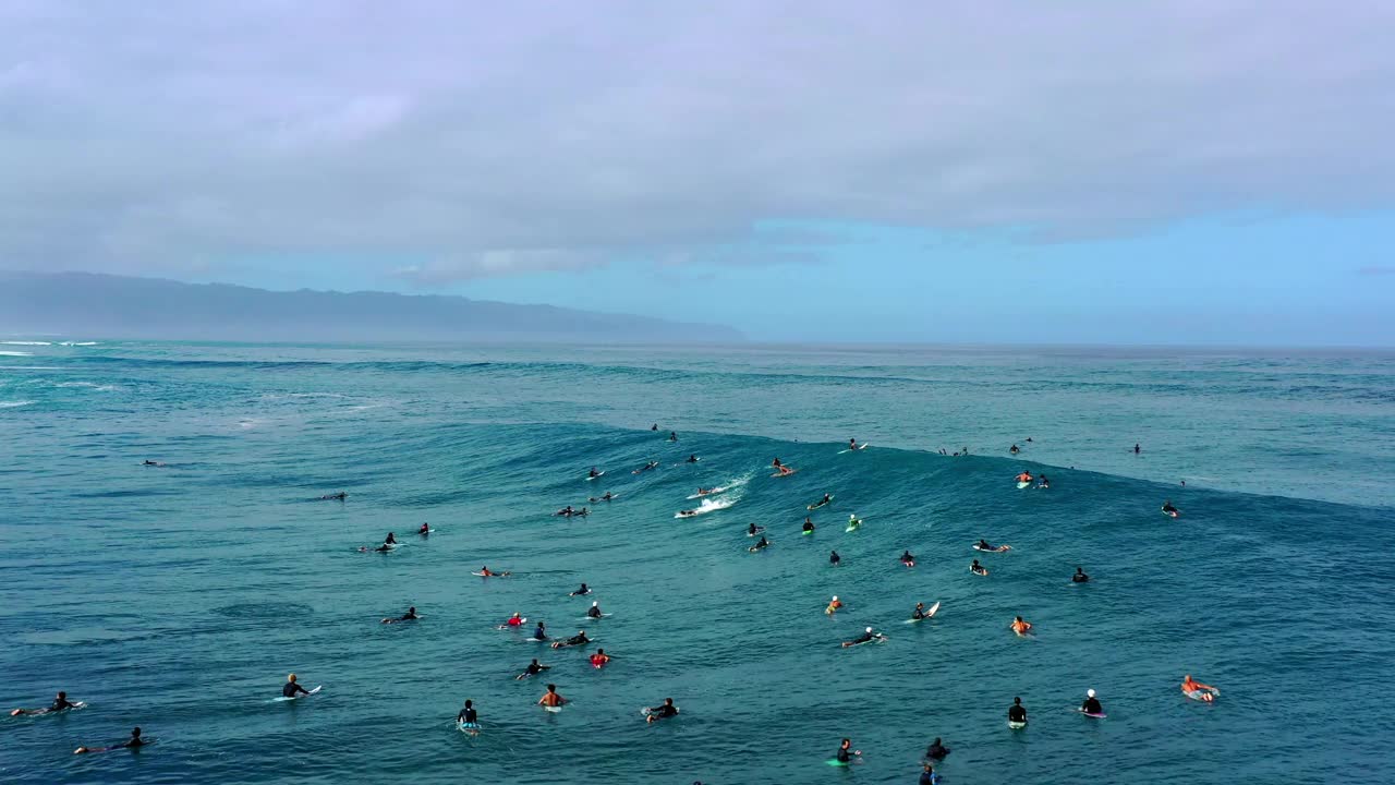 人们在多云天空下的海滩上冲浪的空中平移镜头-夏威夷威基基视频素材