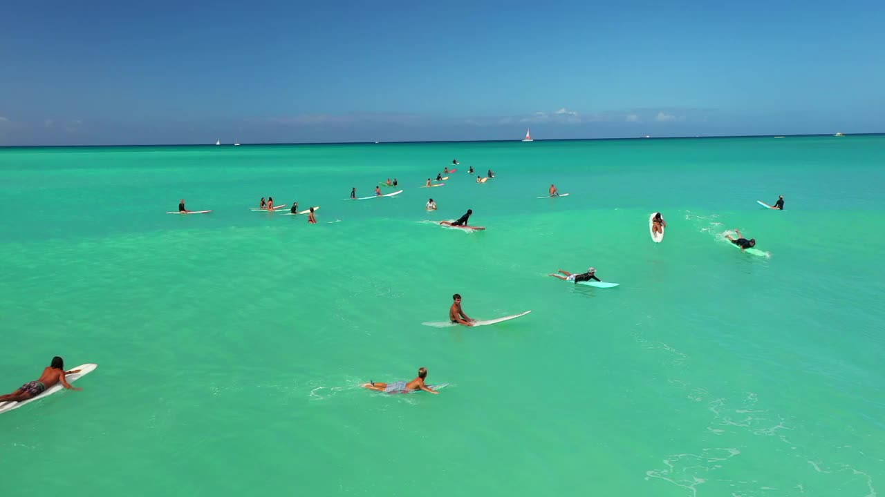 空中平移拍摄的男子在绿色大海的海浪上冲浪，无人机在阳光灿烂的日子里向后飞行——夏威夷瓦胡岛视频素材