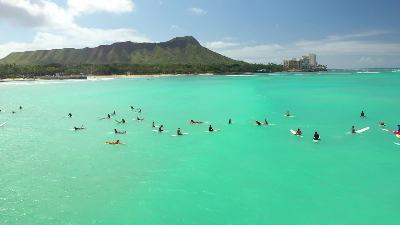 空中平移拍摄的人与冲浪板在绿色的海洋在云下的山-瓦胡岛，夏威夷视频素材