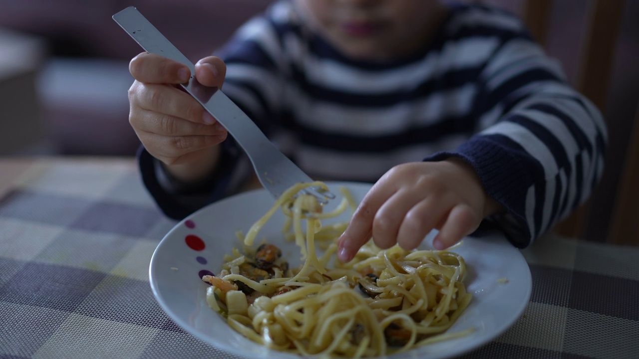 一个可爱的小男孩正在吃意大利面。孩子自己吃面条。2岁小孩吃午饭视频素材