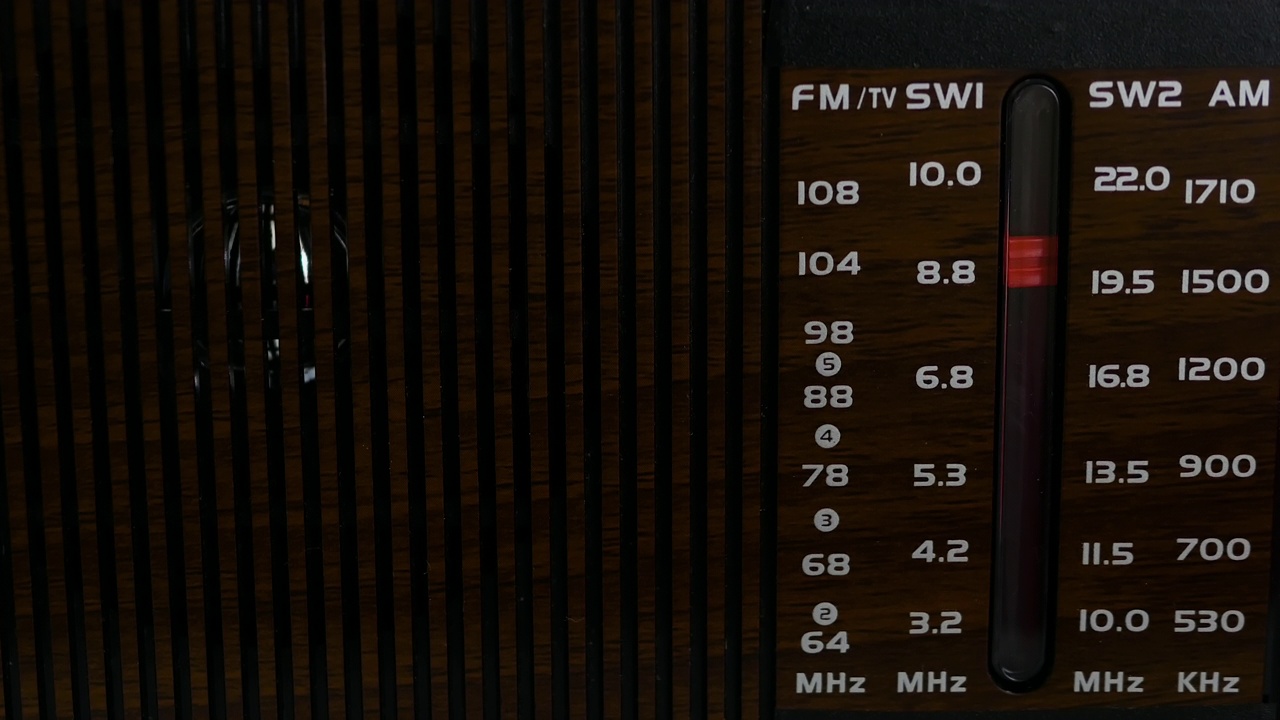 在一张旧木桌上，收音机里播放着无线电波。复古接收器刻度。怀旧的生活方式。把模拟收音机调到一个音阶上。一个男人在用一台旧收音机听新闻视频素材