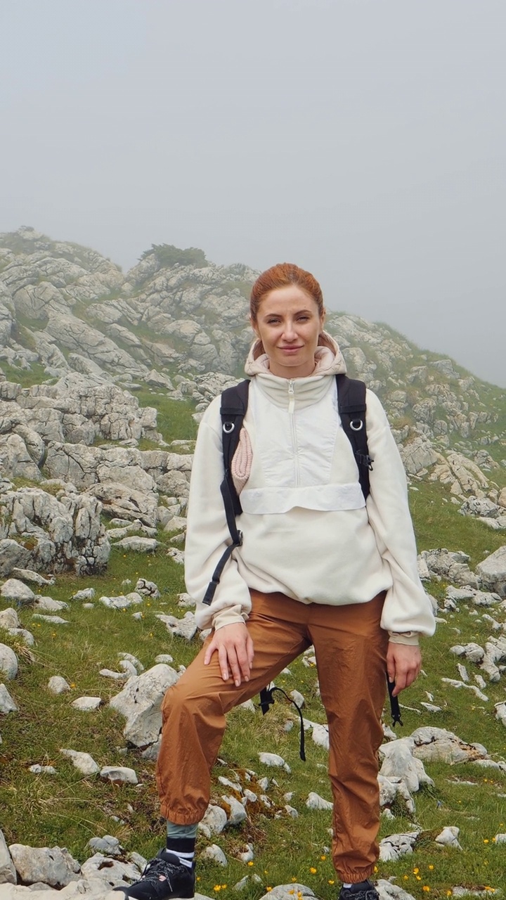 垂直屏幕女人望着镜头，高兴地登上了山顶。视频素材