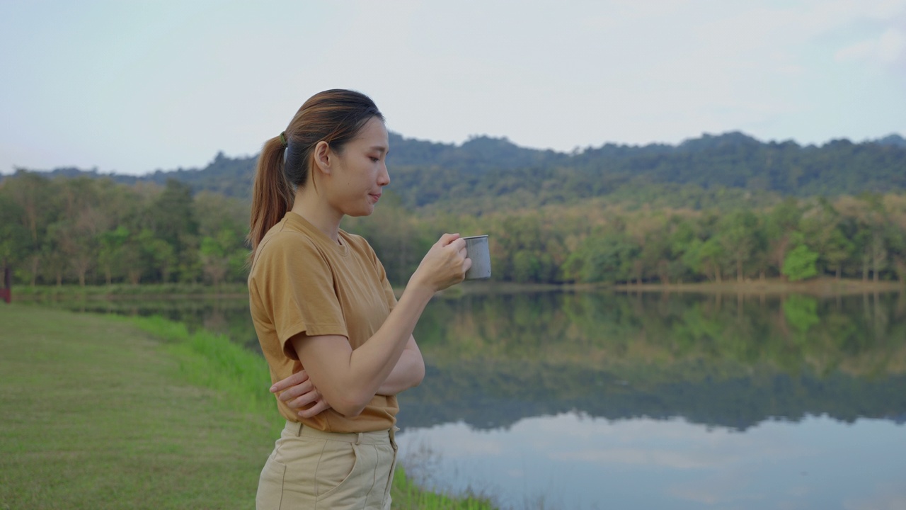 年轻的亚洲女子在湖边喝着早上的咖啡，旅行的想法，放松视频素材