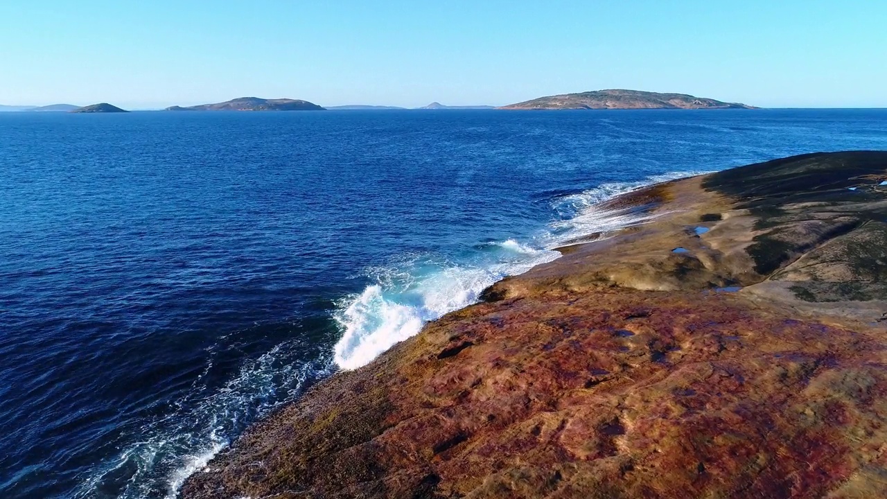 在宽阔的海岸上漂流，海浪冲刷着红色的岩石视频素材