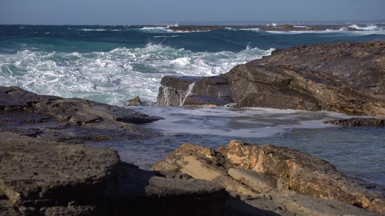 在暴风雨后的一个阳光灿烂的日子里，海浪粉碎海岸线岩石的特写视频下载