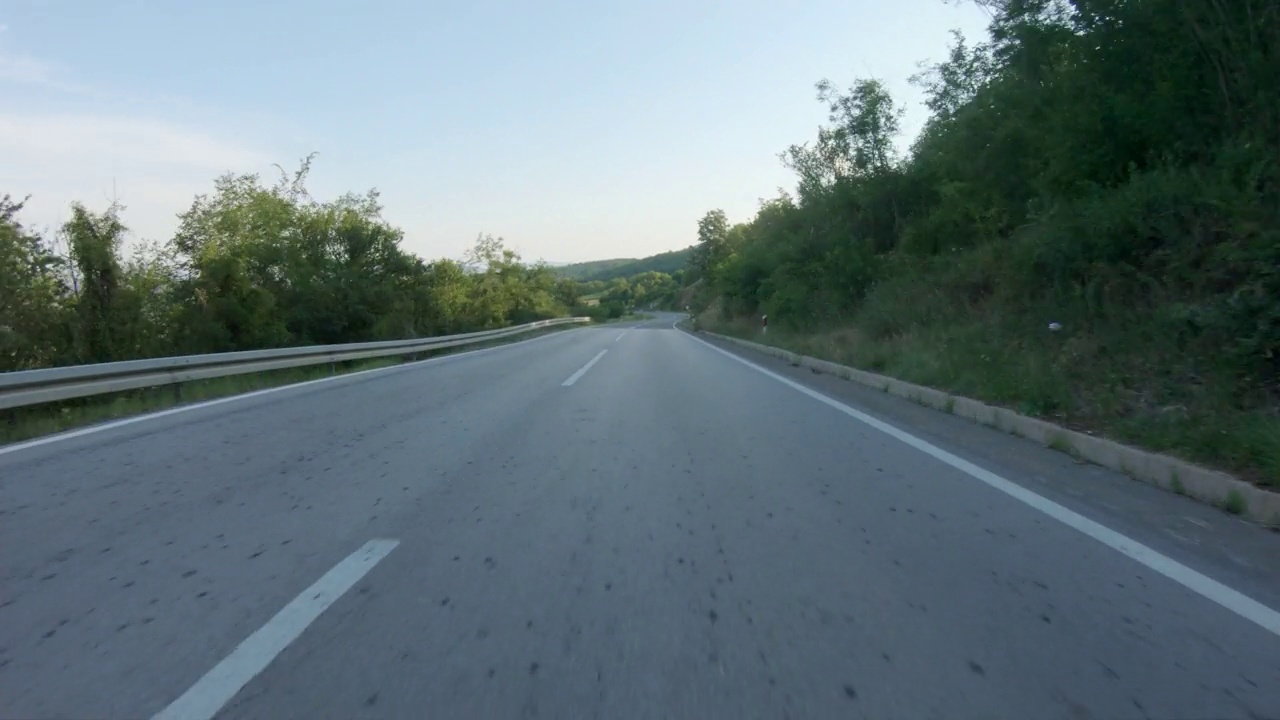 在蜿蜒的山路上快速驾驶汽车或摩托车。山峰和村庄在远处清晰可见。蓝天，夏日时光。观点拍摄视频下载