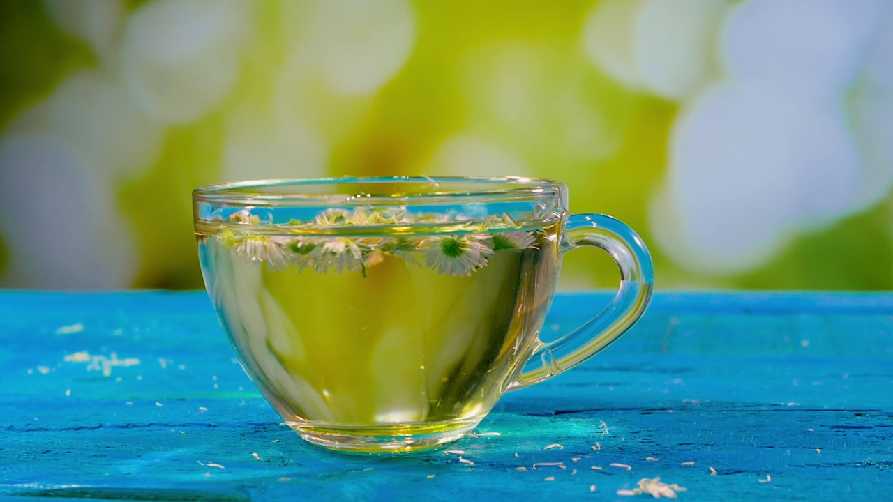 洋甘菊茶在一个透明的玻璃杯。芬芳的药茶与花瓣在夏天的背景。健康饮料视频素材