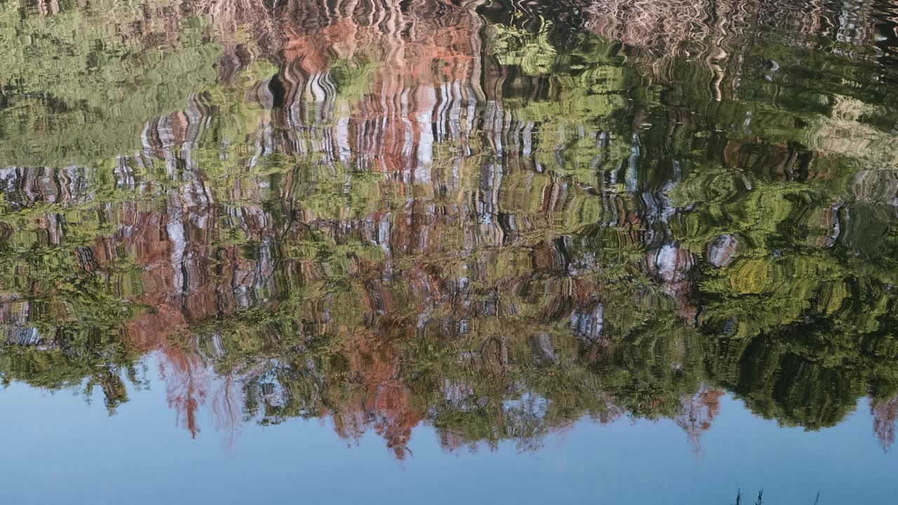 秋日阳光明媚，河里倒影着五彩缤纷的森林，树木随风摇曳，4k慢动作镜头。视频素材