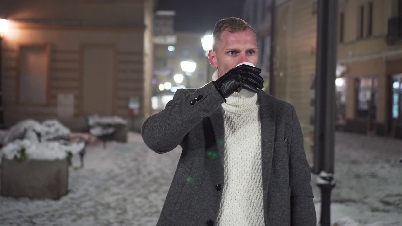 冰冻男子站在冬天下雪的街道上，把外卖咖啡送到嘴边取暖视频素材