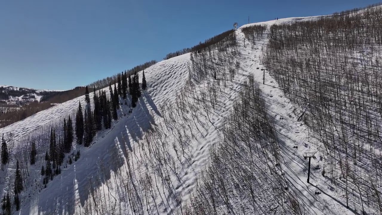 犹他州帕克城的空中v3电影无人机随着电梯飞上雪山的山顶，揭示了滑雪者在阳光明媚的冬天从斜坡上滑下来视频素材