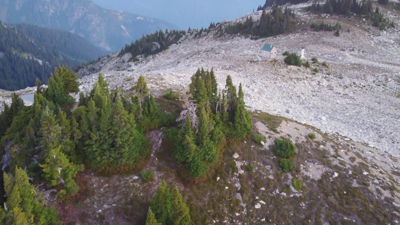 缓慢倾斜的空中无人机拍摄的松树和孤独的小屋在日落的Brew山与雪山在加拿大BC 4K视频素材