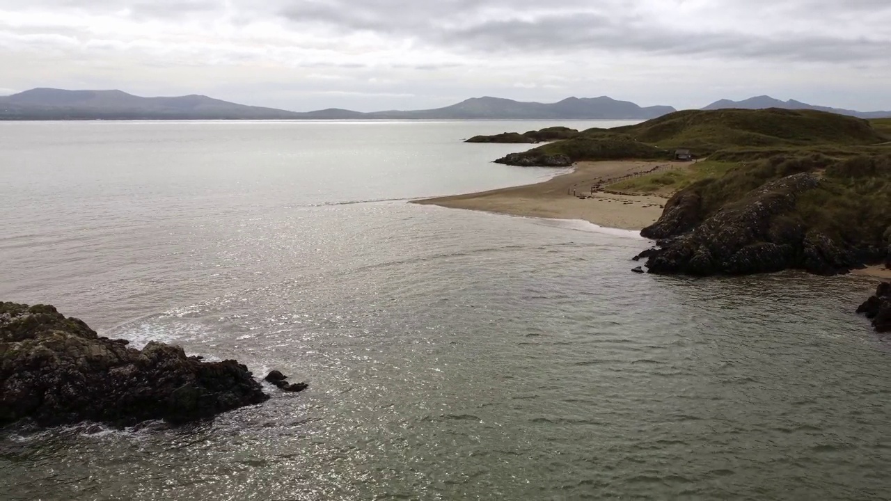 空中上升回到Ynys Llanddwyn岛安格尔西海岸步行道与斯诺登尼亚山脉横跨爱尔兰海视频素材