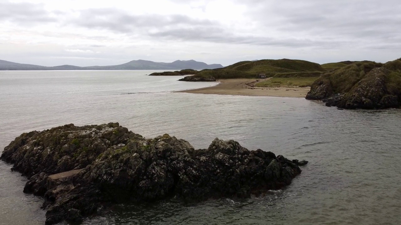 鸟瞰Ynys Llanddwyn岩石岛安格尔西海岸步行小径与斯诺登尼亚山脉横跨爱尔兰海视频素材