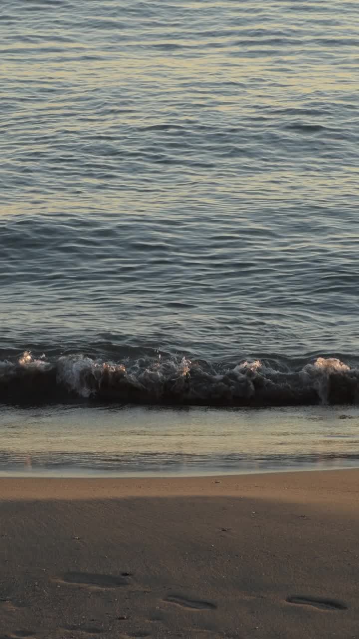 日落时分，小浪涌向海滩。4 k垂直视频素材