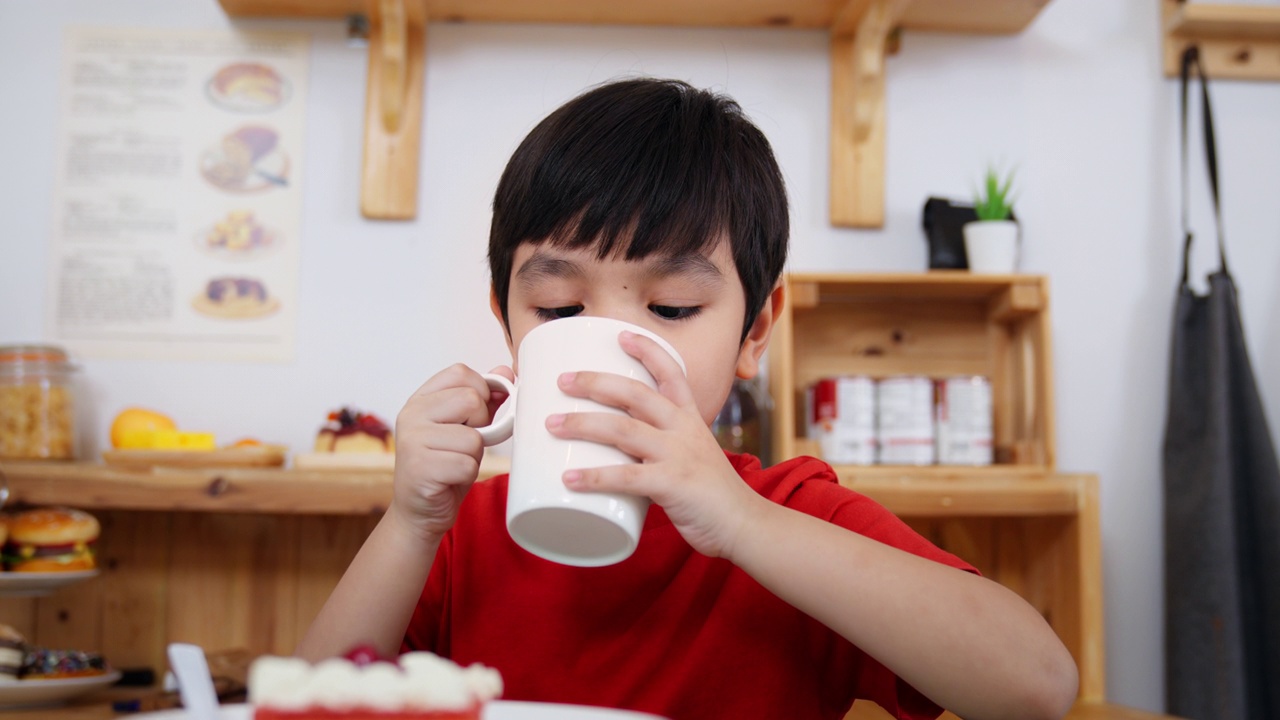 小可爱的男孩拿着一杯牛奶在厨房里笑着喝早餐。孩子舔着嘴唇。家庭生活保健药食品。儿子喝完一杯牛奶。积极的孩子和享受与家人吃饭视频素材