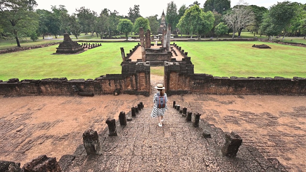 一名亚洲游客从Wat Chang Lom寺主楼的楼梯上走下来，是一座巨大的钟形佛塔，位于素可泰省的Si Satchanalai历史公园。视频素材