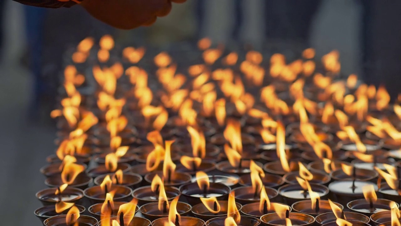 男人在蜡烛上祈祷温暖他的手。在佛教圣地博德哈纳斯，祈祷的手和燃烧的蜡烛。加德满都,尼泊尔。慢镜头视频素材