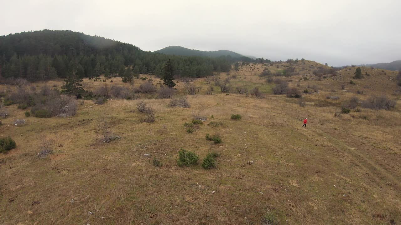 秋天的一天，穿着红色运动服的女孩在以山林为背景的田野里奔跑视频素材