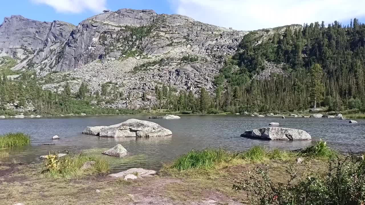 一个美丽的湖泊，在高山的映衬下，巨石突出在水面上。视频素材