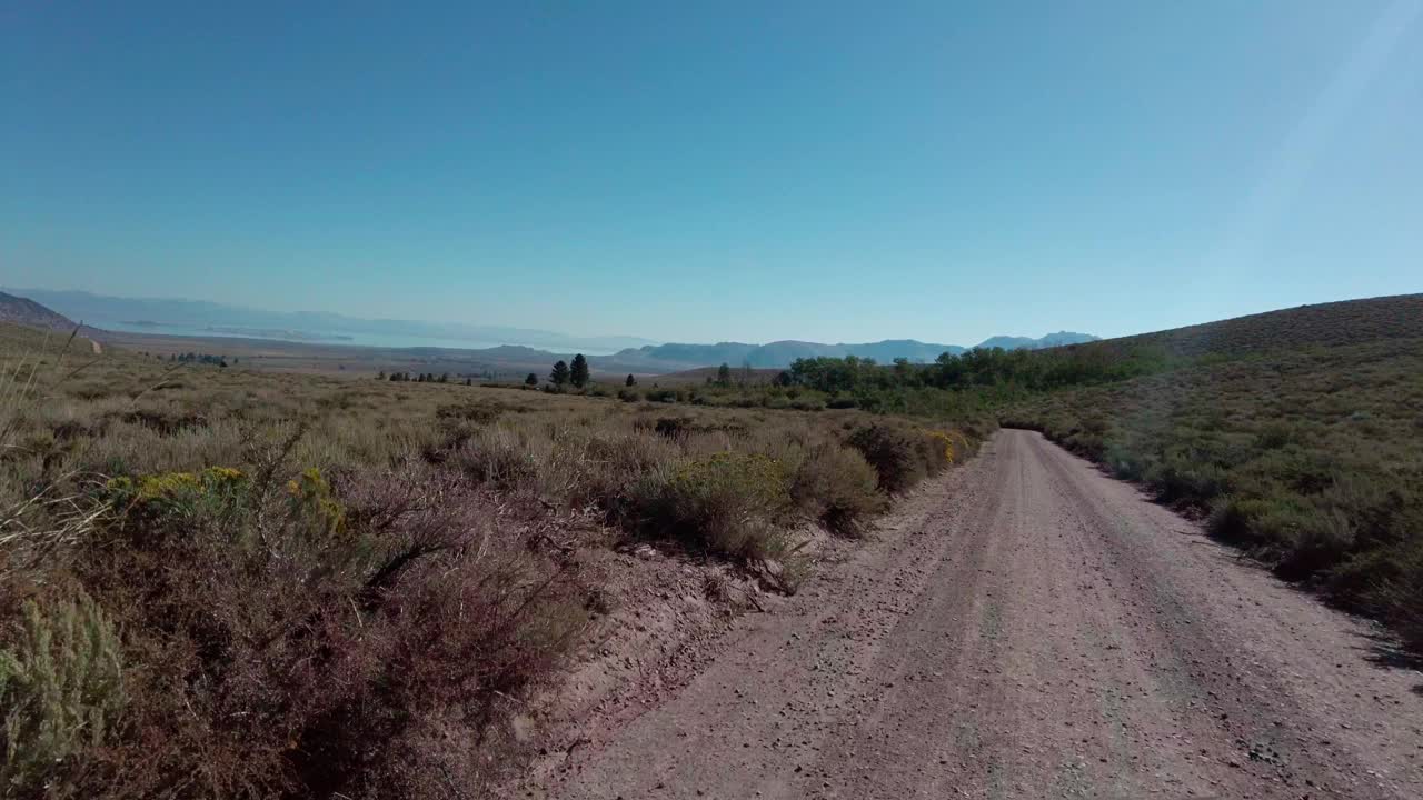 在一个阳光明媚的日子里，一条未铺设的道路在草地上，山脉在地平线上视频素材