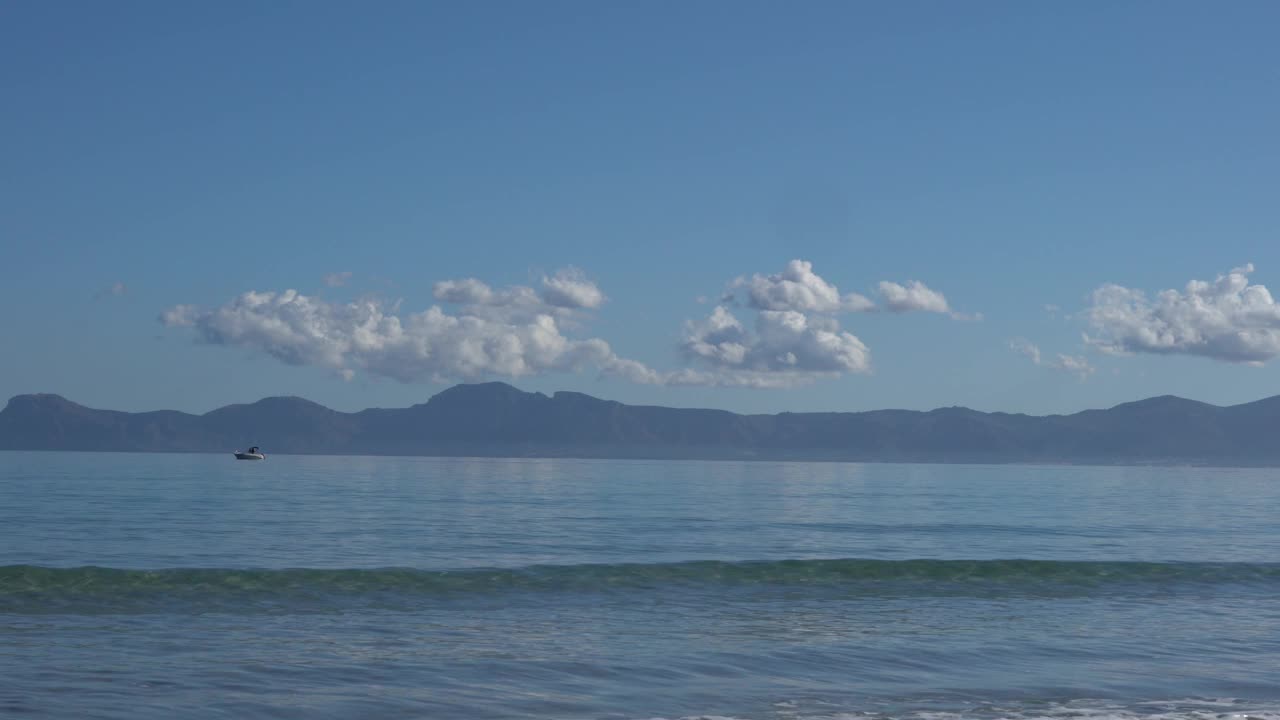 小船沿着宁静的海洋航行，从海滩上看，背景是山脉视频下载