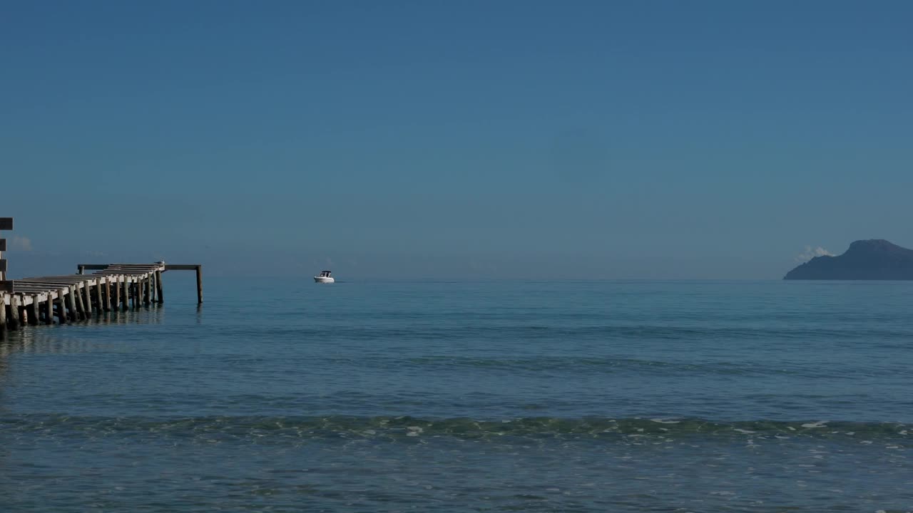 小船沿着宁静的海洋航行，从海滩上看，背景是山脉视频下载