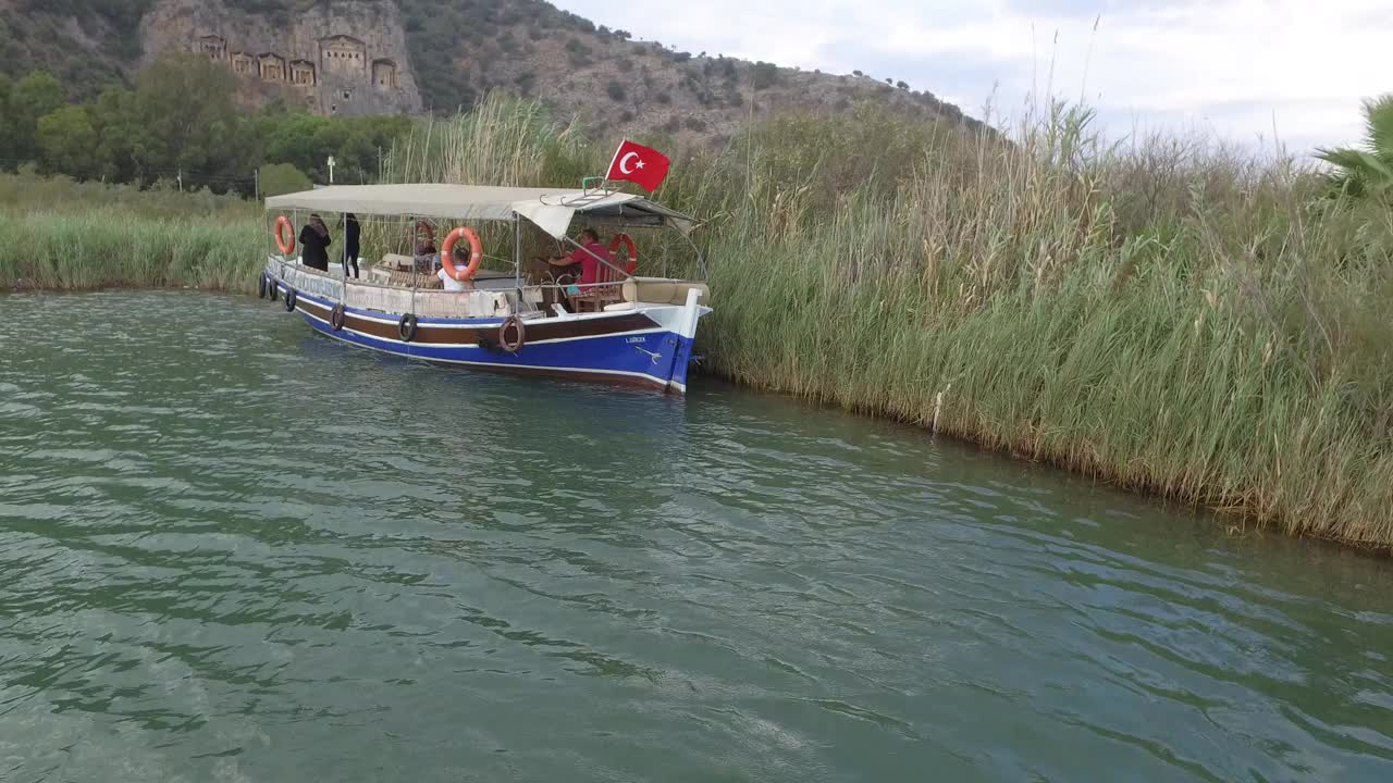 拍摄了一艘木制的旅游船在水中，山和长长的草药视频素材