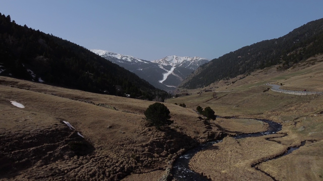 在阳光明媚的夏天，流过安道尔山谷的小溪，背景是白雪皑皑的山脉，比利牛斯在西班牙。空中向后和天空为复制空间视频素材