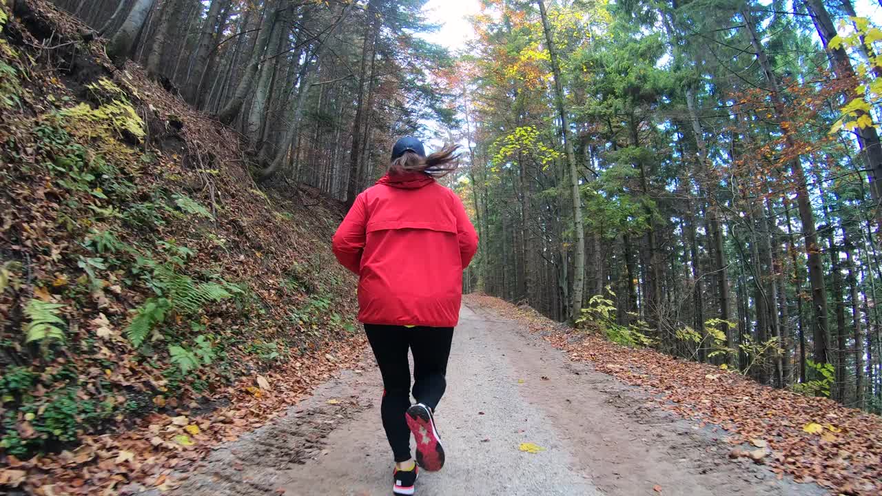 穿着红色运动服的年轻女子在树林间的狭窄道路上奔跑视频素材