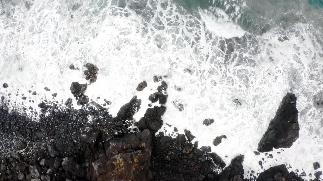 泡沫的海浪冲刷着海岸悬崖下的鹅卵石和岩石。视频素材