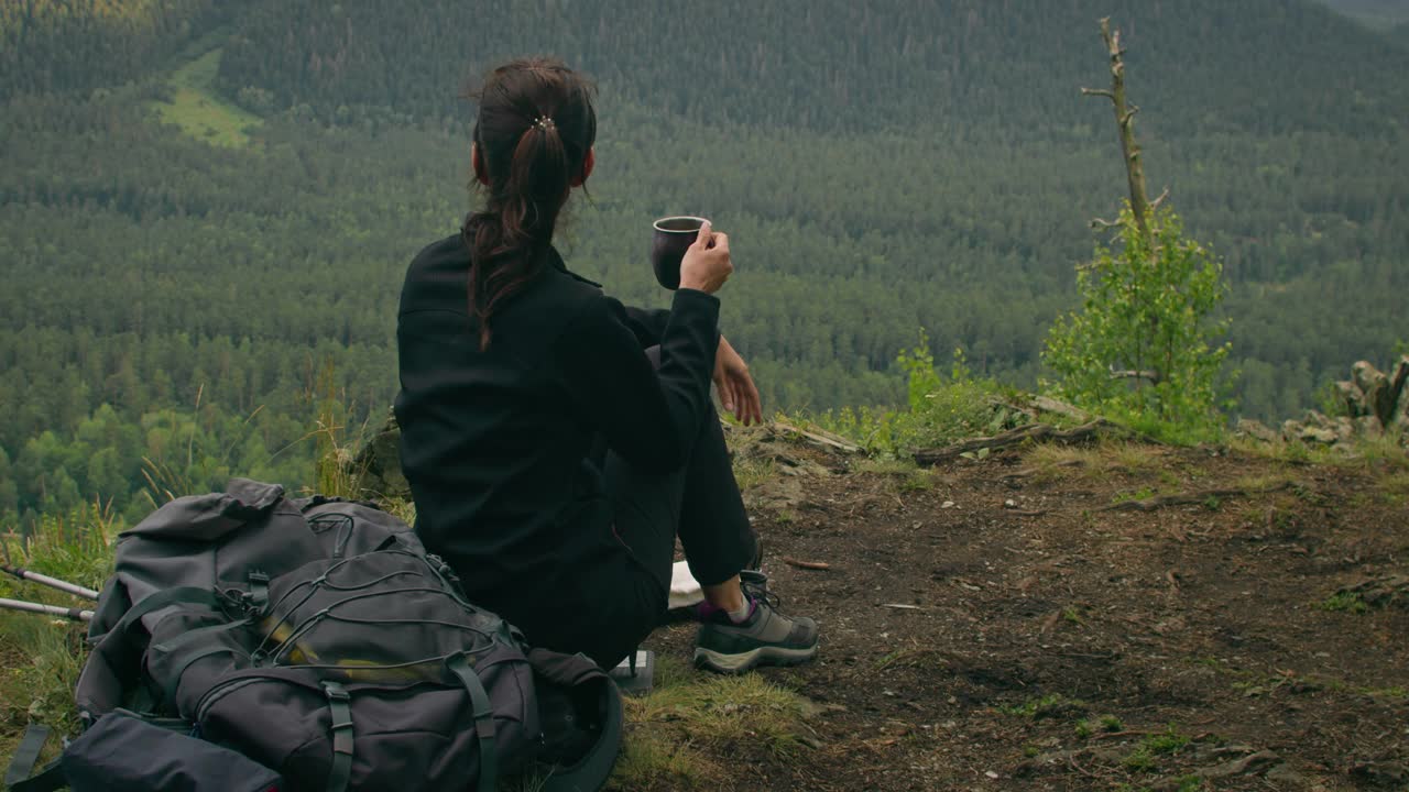 女徒步者喝茶休息在徒步山看山谷视频素材