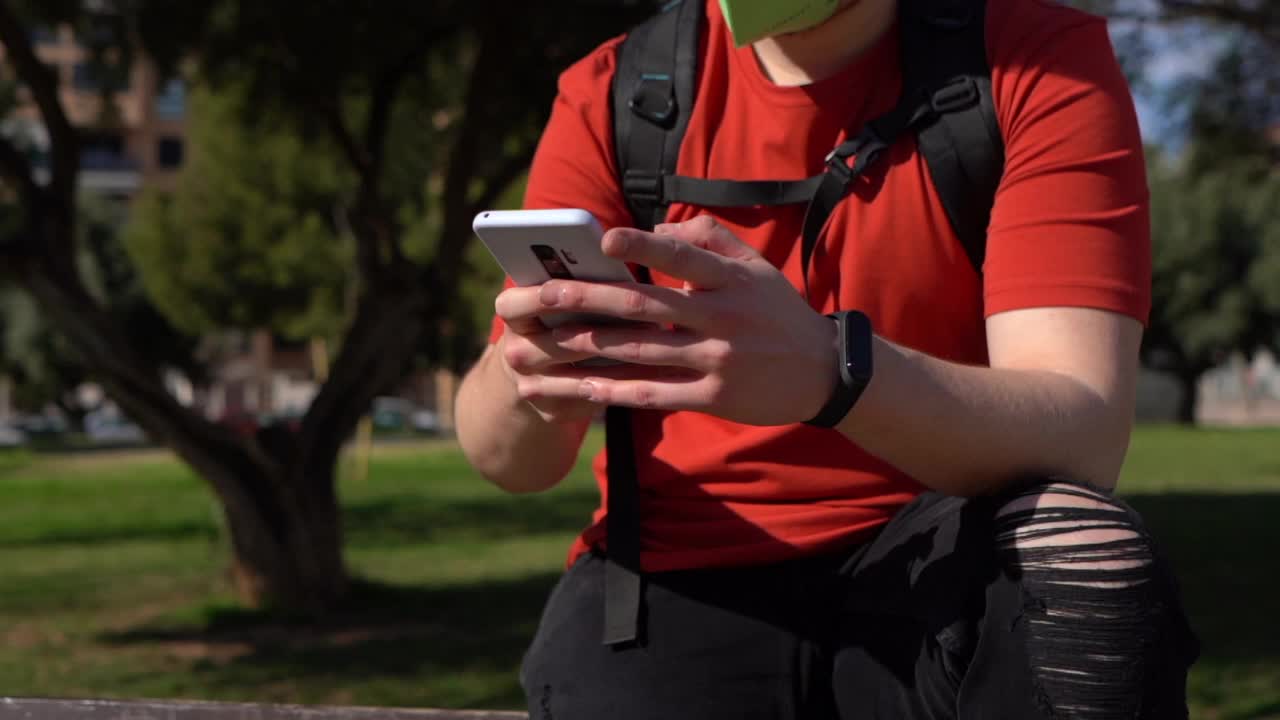 白人男性，戴着面具穿着红衬衫戴着面具在公园里打电话视频素材