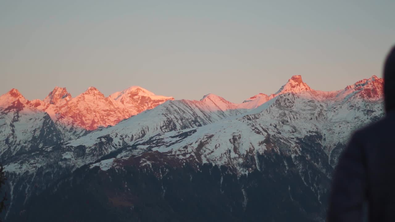 日落时分，一名散焦的徒步旅行者在雪峰前举起手臂，俯瞰白雪覆盖的喜马拉雅山峰。徒步旅行者在看到日落后举起了拳头。视频素材