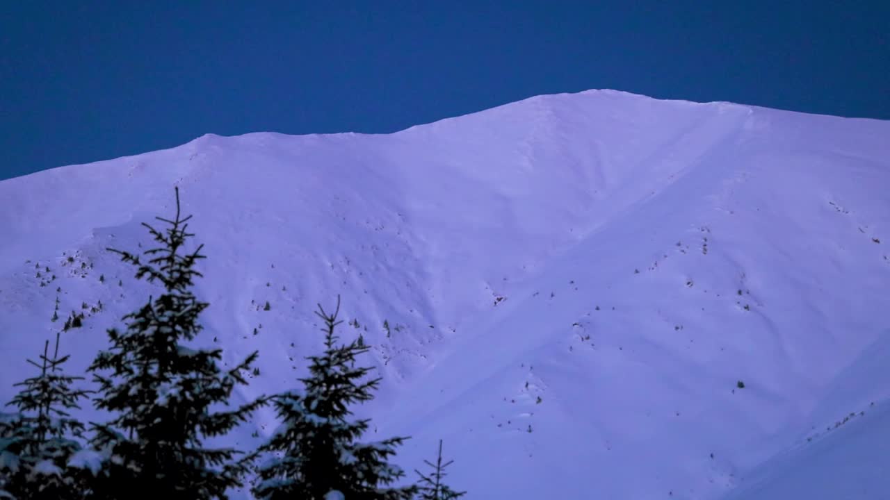 深蓝色的夜空下，白雪覆盖的小山风景优美视频素材