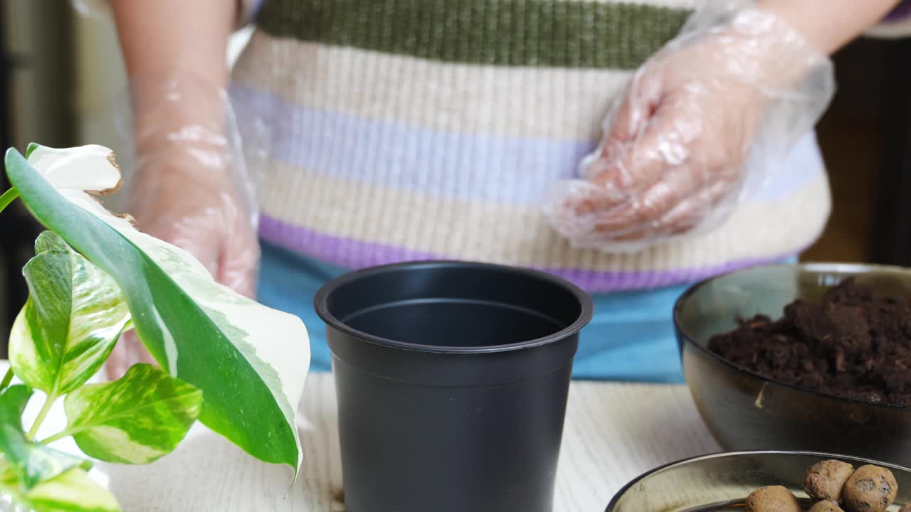 一名妇女将排水沟的石头和土壤倒进花盆里种植植物。视频素材