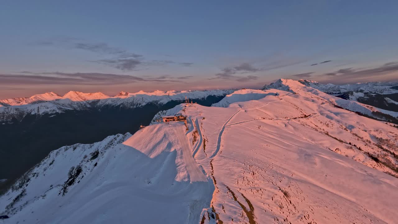 滑雪场位于雪山山脊山顶，周围是粉金色的夕阳视频素材