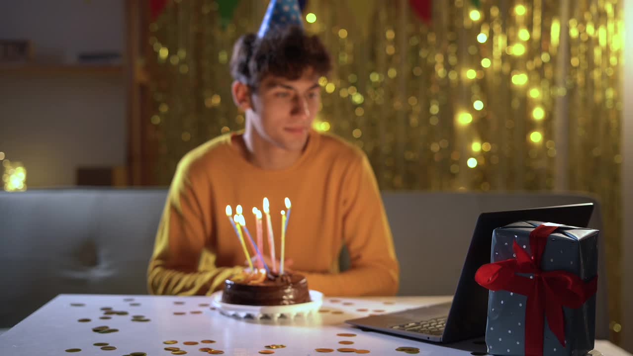 虚拟的庆祝活动。快乐的穆斯林男子戴着派对帽在网上庆祝生日，用笔记本电脑与朋友和家人视频通话，手里拿着蛋糕视频素材