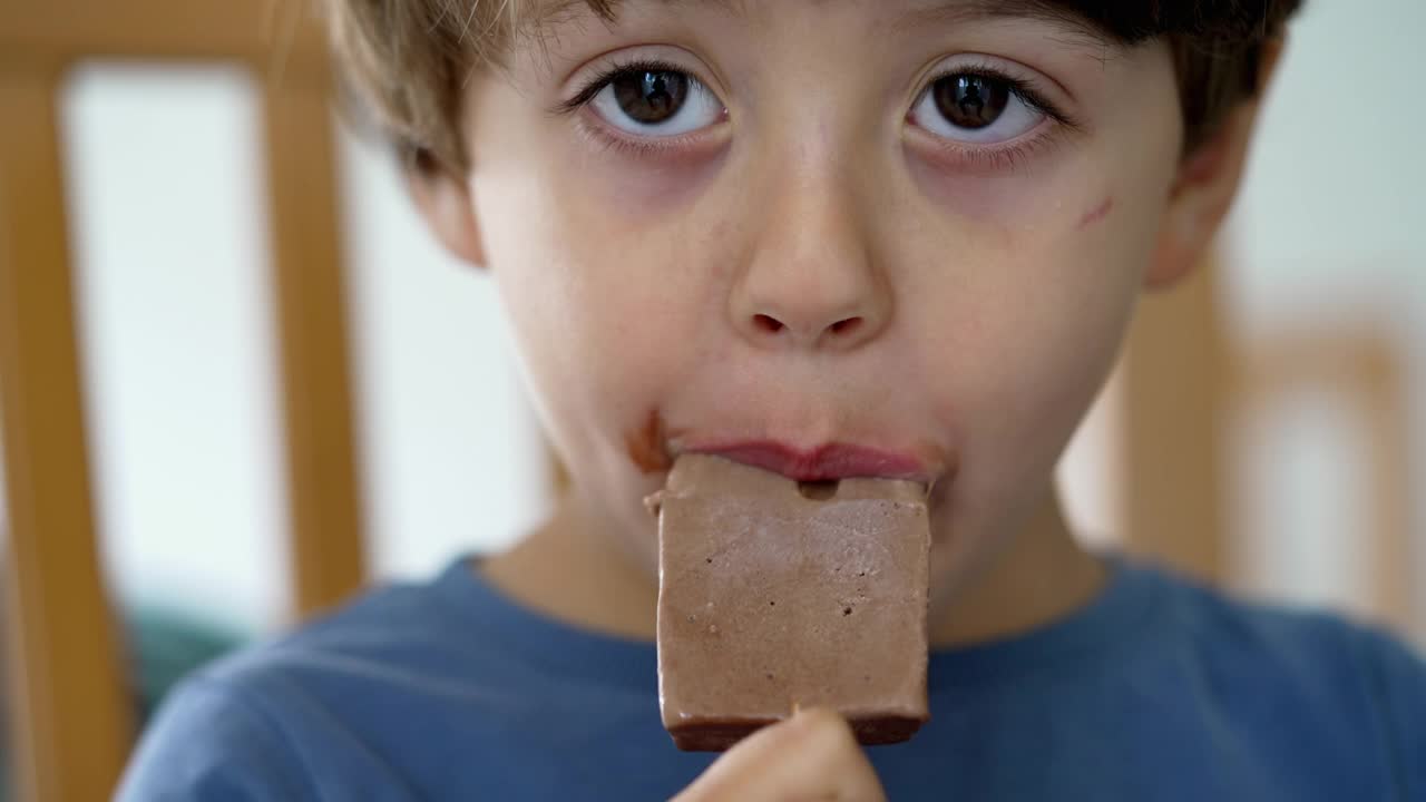 孩子的嘴里塞满了巧克力冰淇淋。小男孩吃了一口冰淇淋甜点视频素材