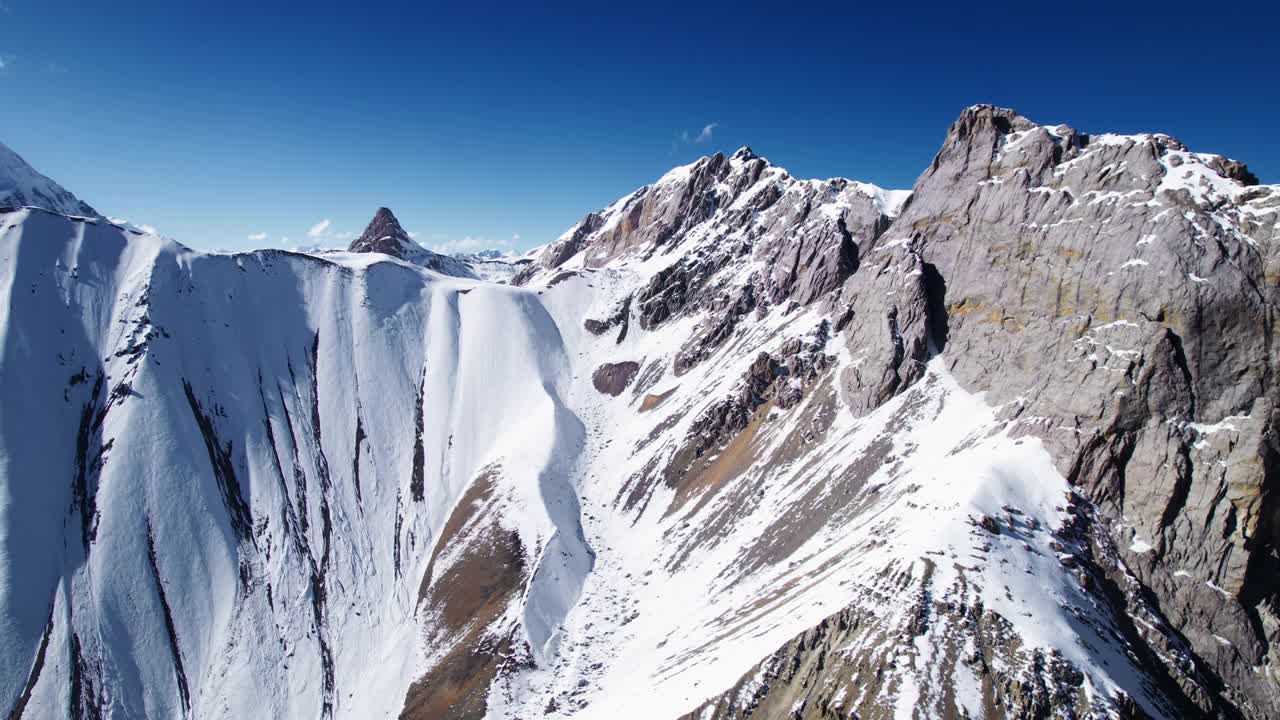 在明亮的阳光下，在晴朗的天空下，山脉的壮丽鸟瞰图。白雪皑皑的山峰。无人机拍摄的山区画面视频素材