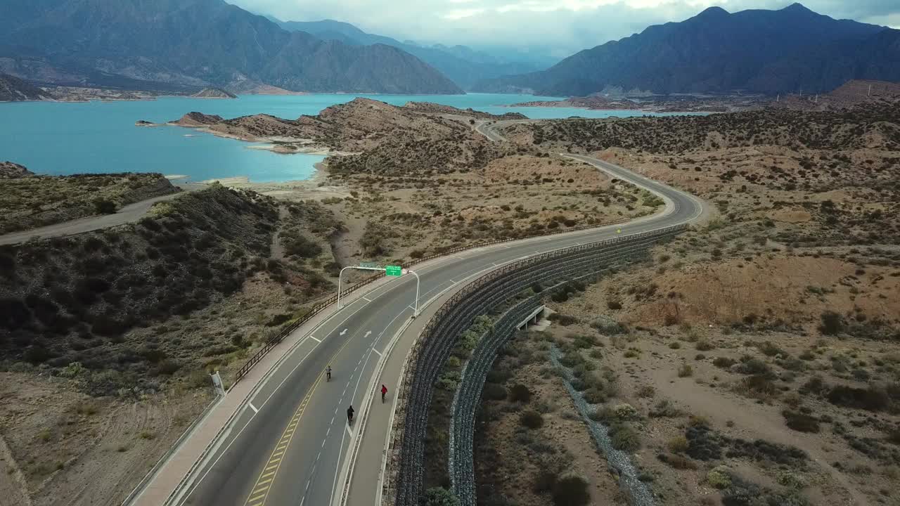 骑自行车的人在一条被群山环绕的蓝色河流的风景优美的道路上-门多萨波特雷利洛斯大使馆-阿根廷视频素材