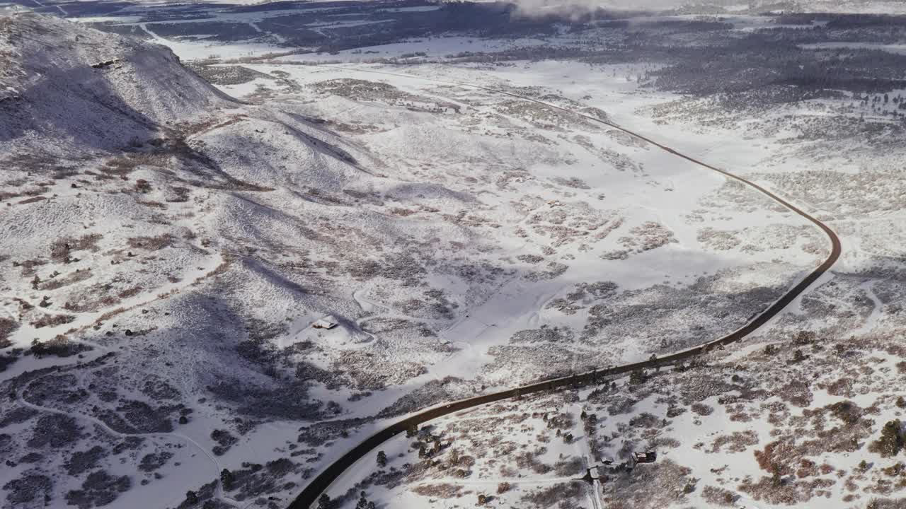 拉回起重机拍摄的积雪覆盖的冬季山地景观与道路和汽车在科罗拉多地区视频素材