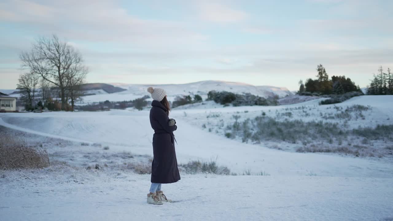 穿着冬衣的女子站在雪地里，显示出寒冷的迹象视频素材