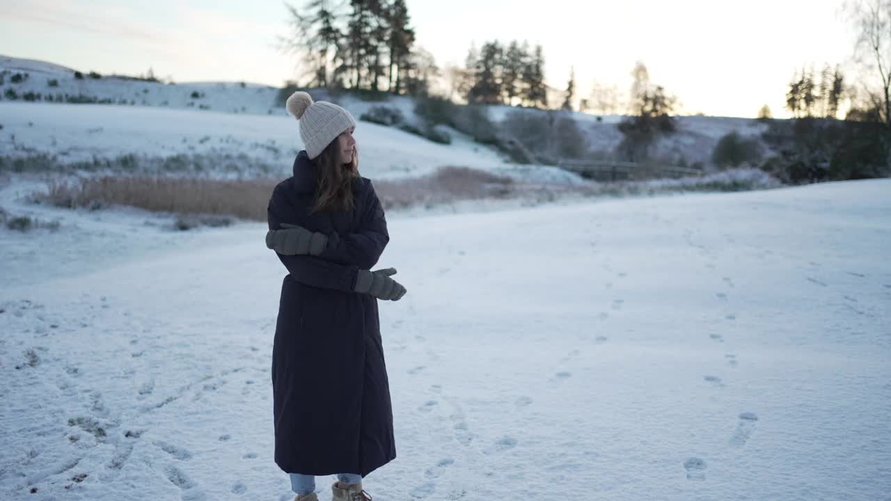 穿着冬衣的女子站在雪地里，显示出寒冷的迹象视频素材